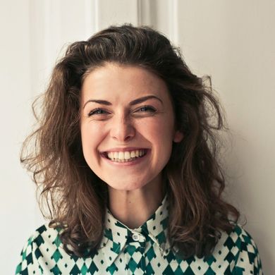 Woman with brown hair and a patterned shirt smiles broadly.