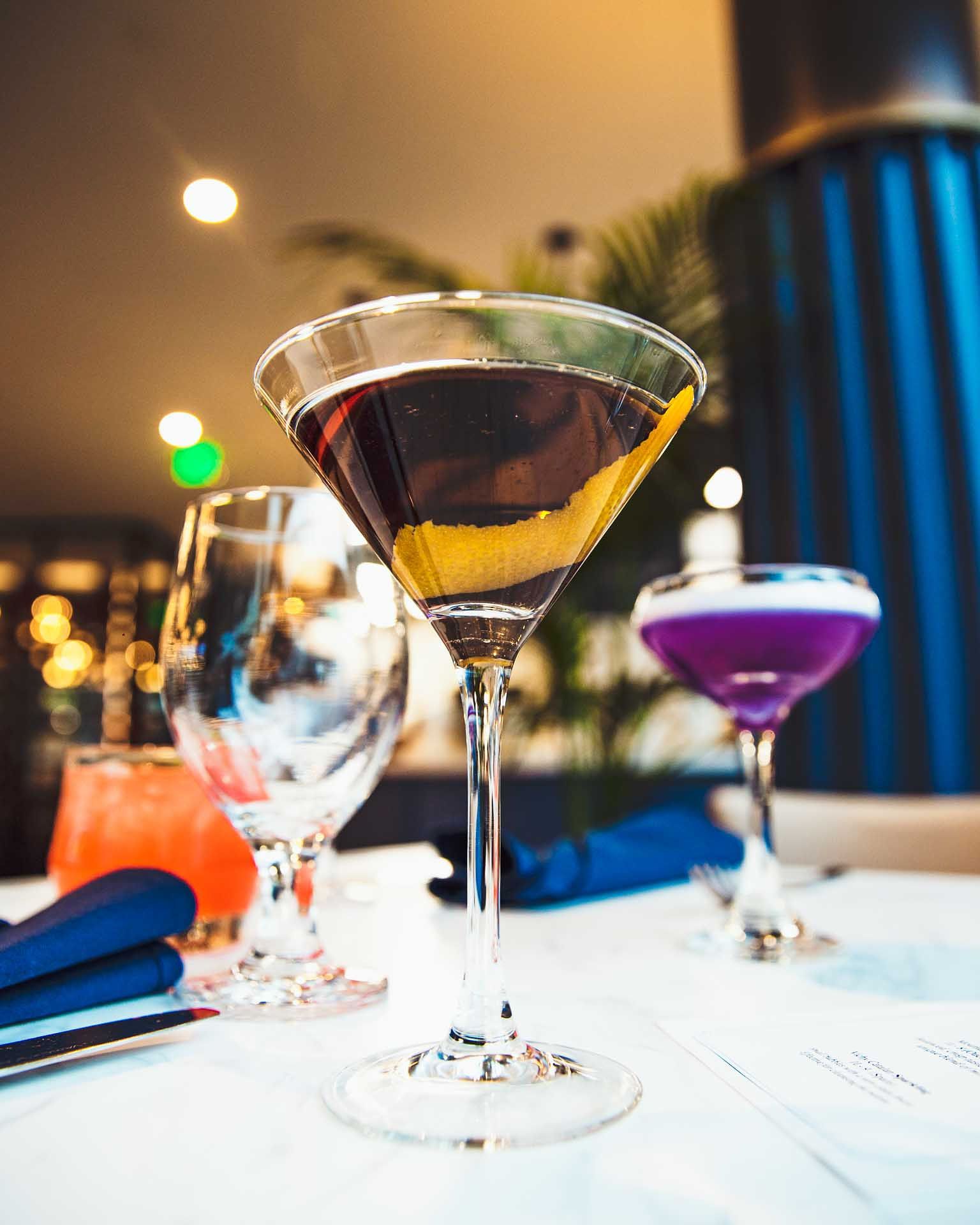 a martini with a orange peel on top sits on a table