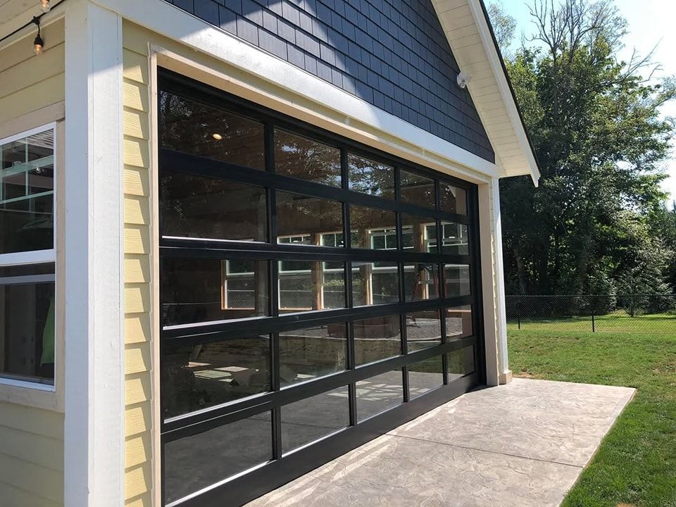 Modern black-framed glass garage door on a light-sided house beside a concrete driveway