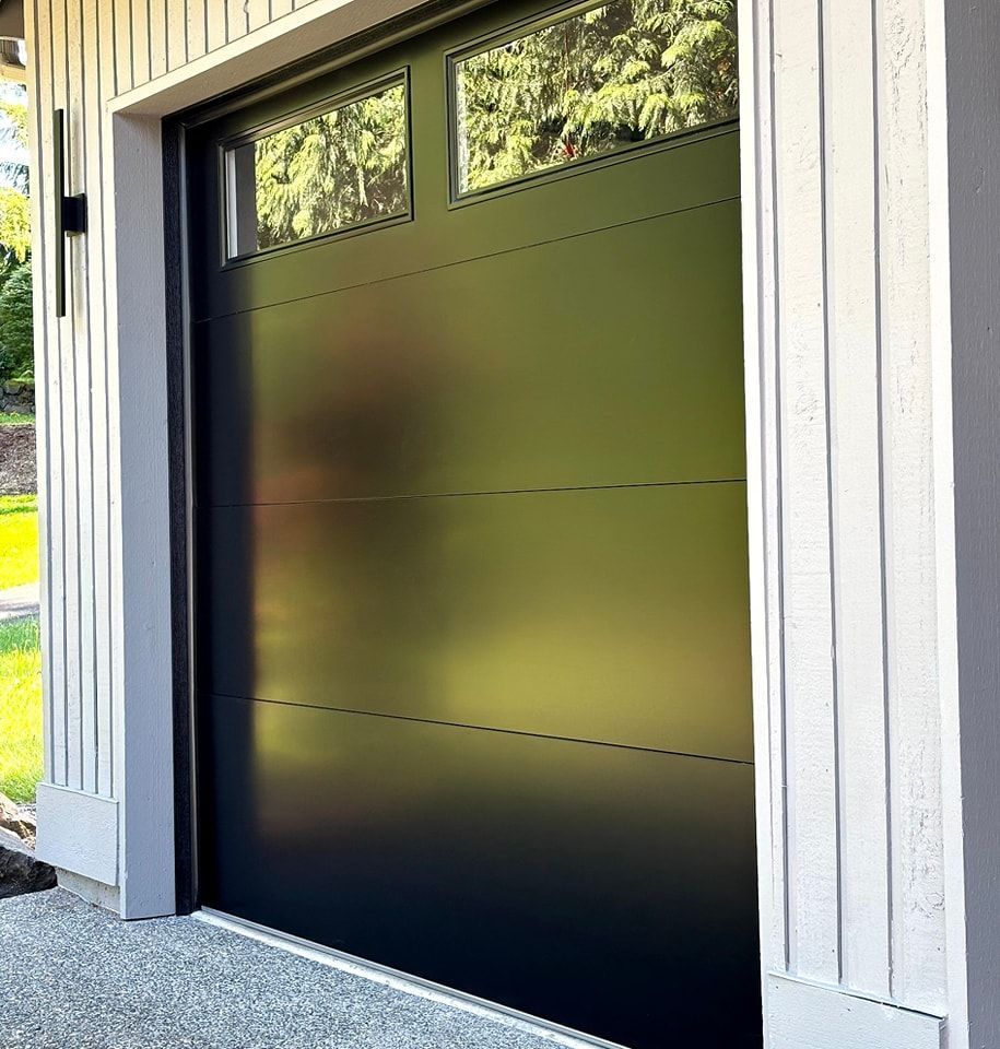Modern black garage door with frosted upper windows and white siding trim