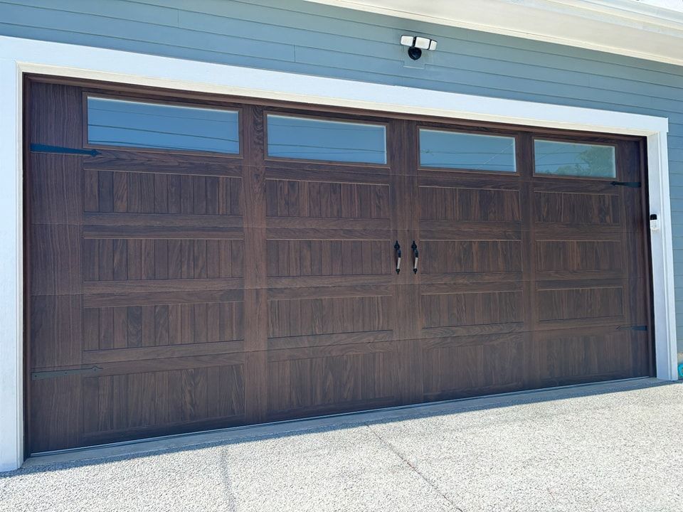 Two-car brown garage door with small windows on a light blue house exterior