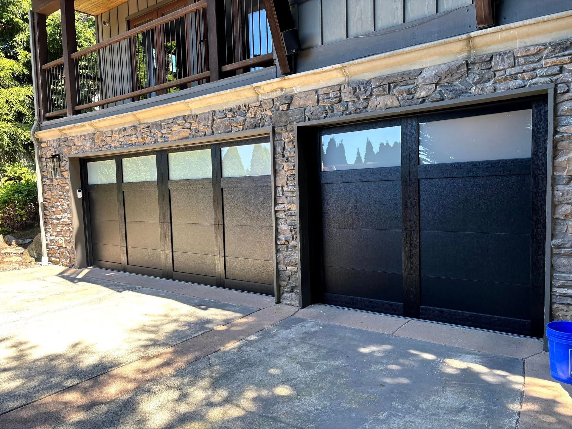 Stone house exterior with large dark tinted windows and garage doors along a concrete driveway