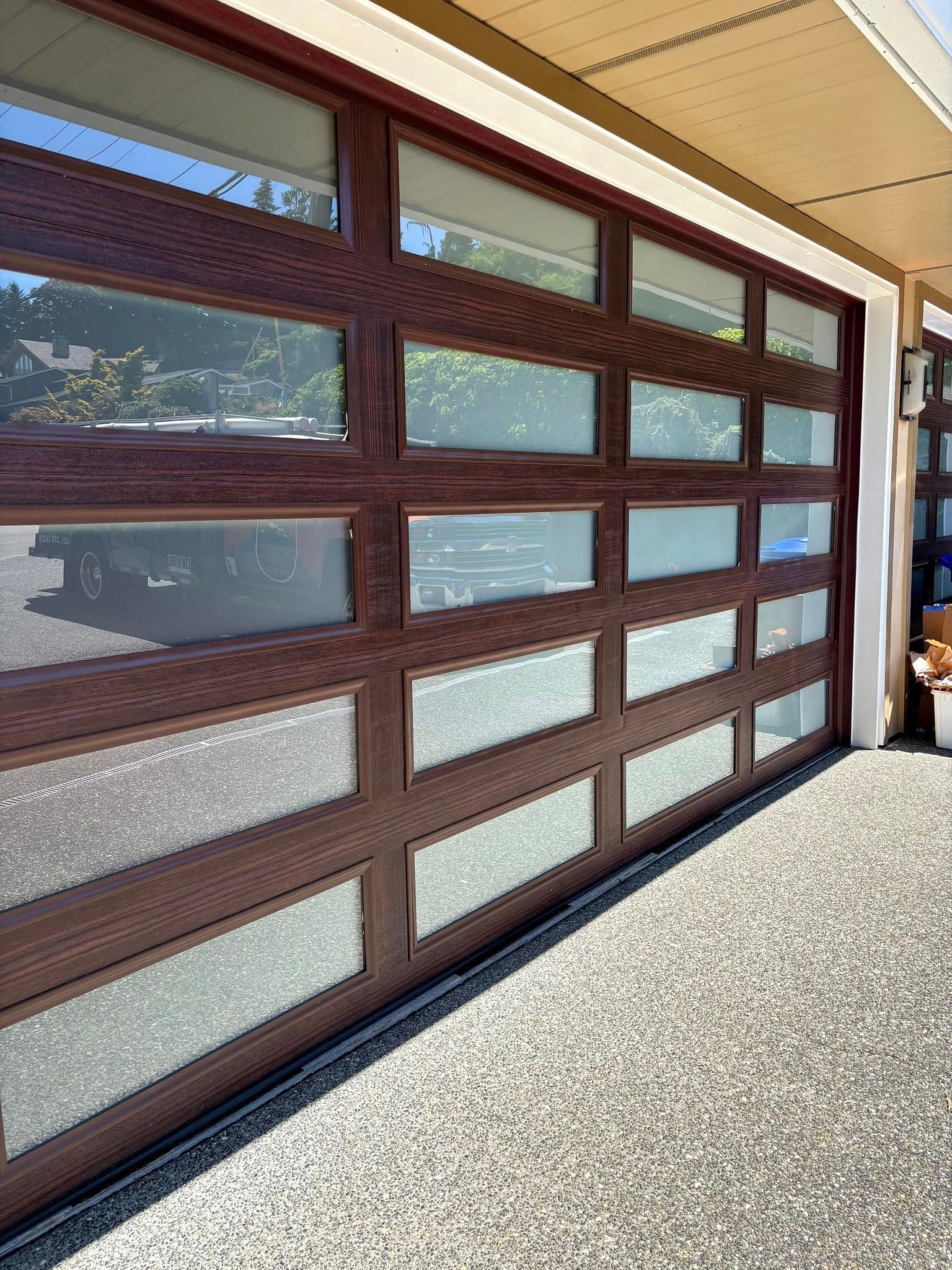 Brown-framed frosted window panels along a sunlit exterior walkway under a covered roof.