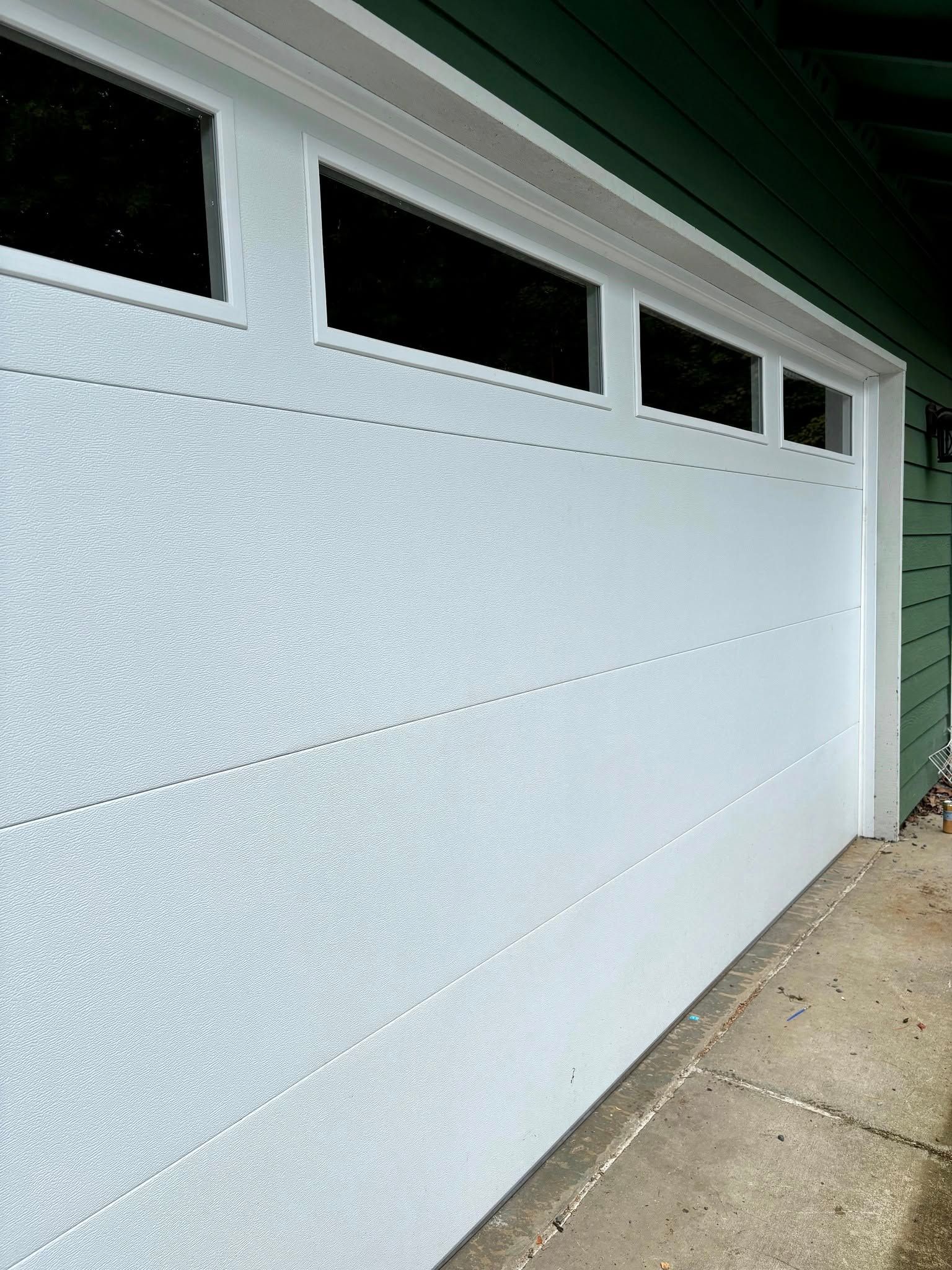 White garage door with narrow windows beside a driveway and house siding