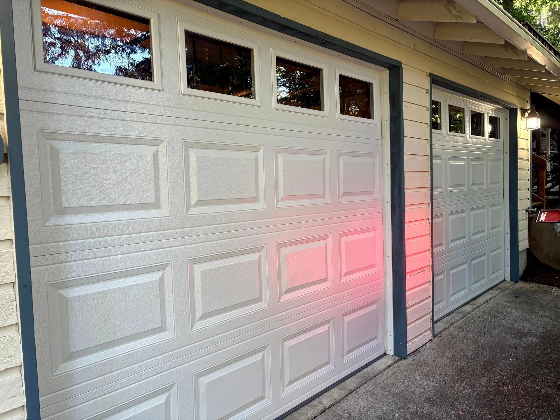 Two white garage doors under an eave, with pink light reflecting on the right door.