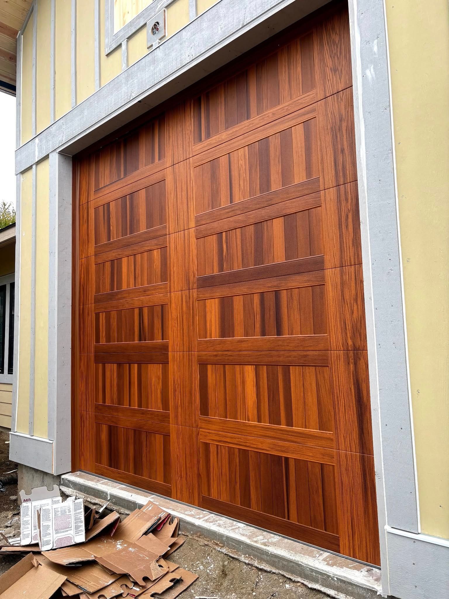 Large wooden double doors installed in a gray building facade, with construction debris on the ground.
