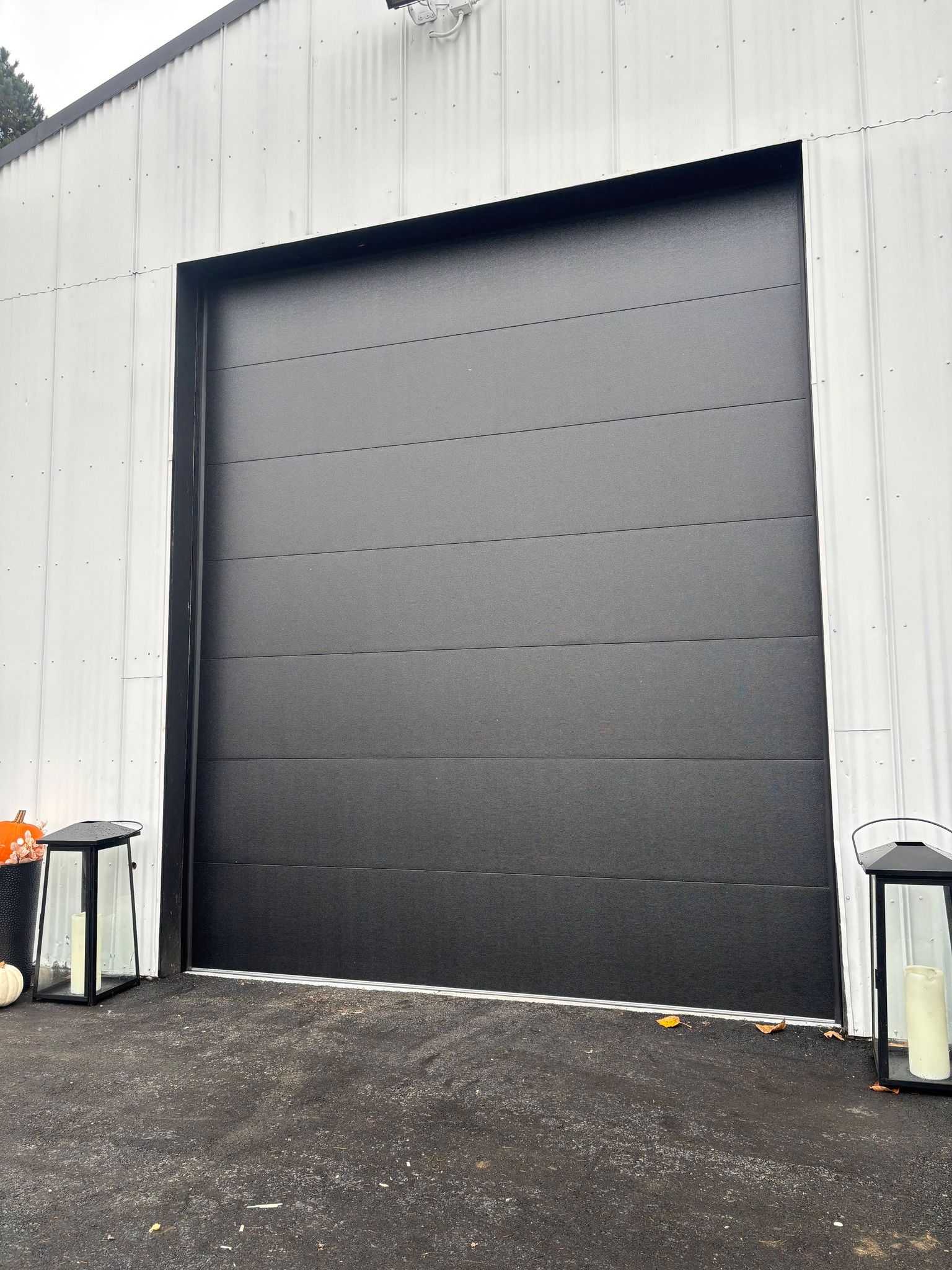 Gray industrial roll-up door set in a white warehouse wall with wet pavement in front