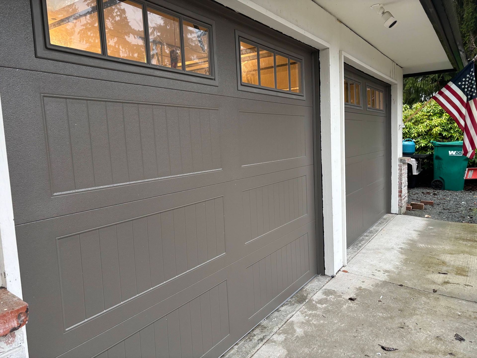 Two-car garage with brown doors beside a driveway and an American flag hanging nearby