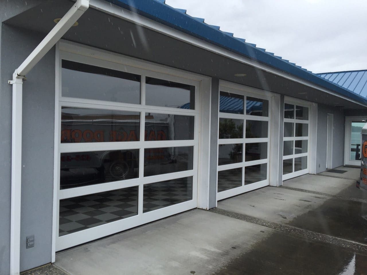 Gray garage bays with white-framed glass doors along a wet concrete driveway