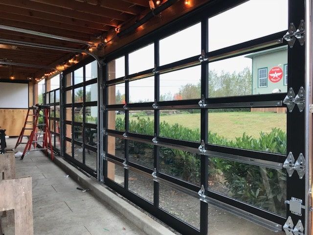Garage with black-framed glass doors, wooden ceiling beams, and a ladder inside.