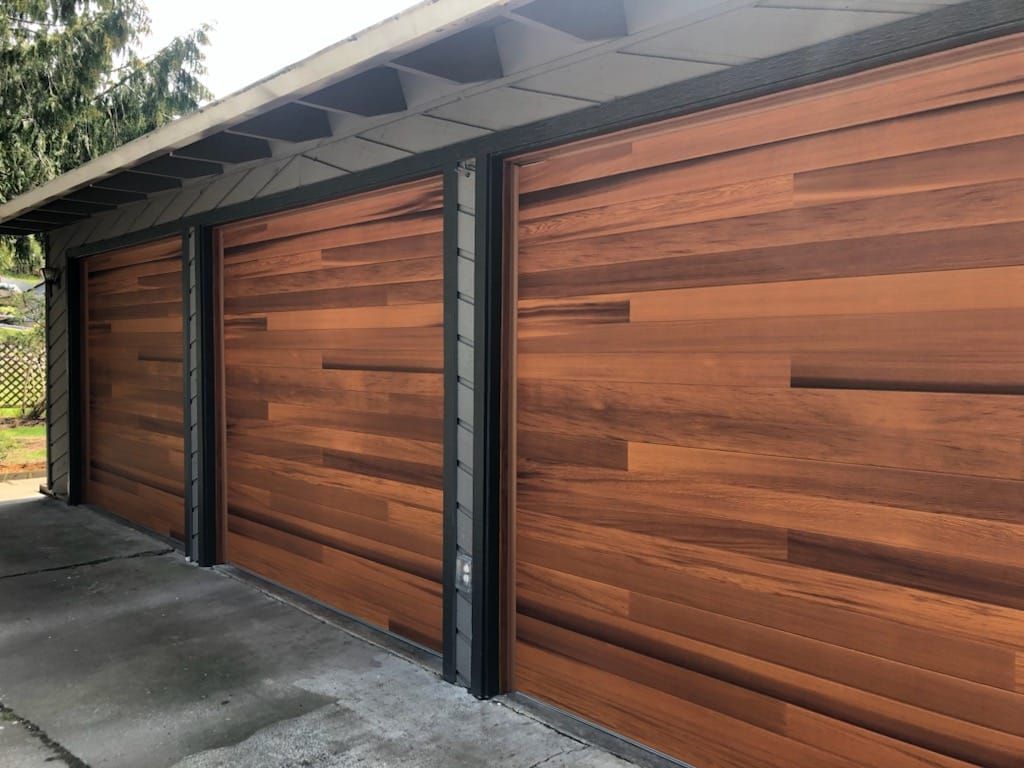 Three wood-paneled garage doors with black frames on a modern carport