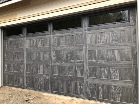 Gray wooden garage doors on a house exterior, with small windows along the top.