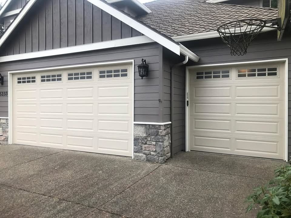 Two-car white garage doors on a gray house with stone accents and a concrete driveway