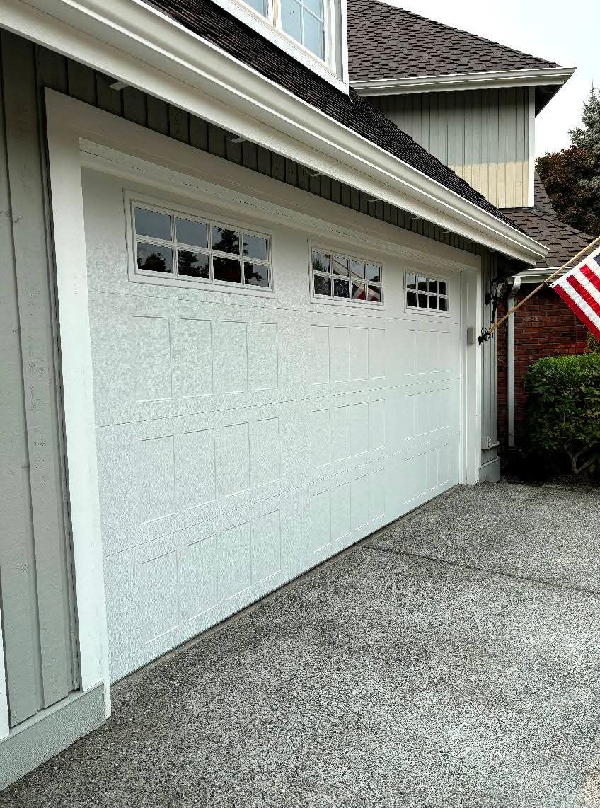 White garage door with small windows beside a house, with a gravel driveway and an American flag.