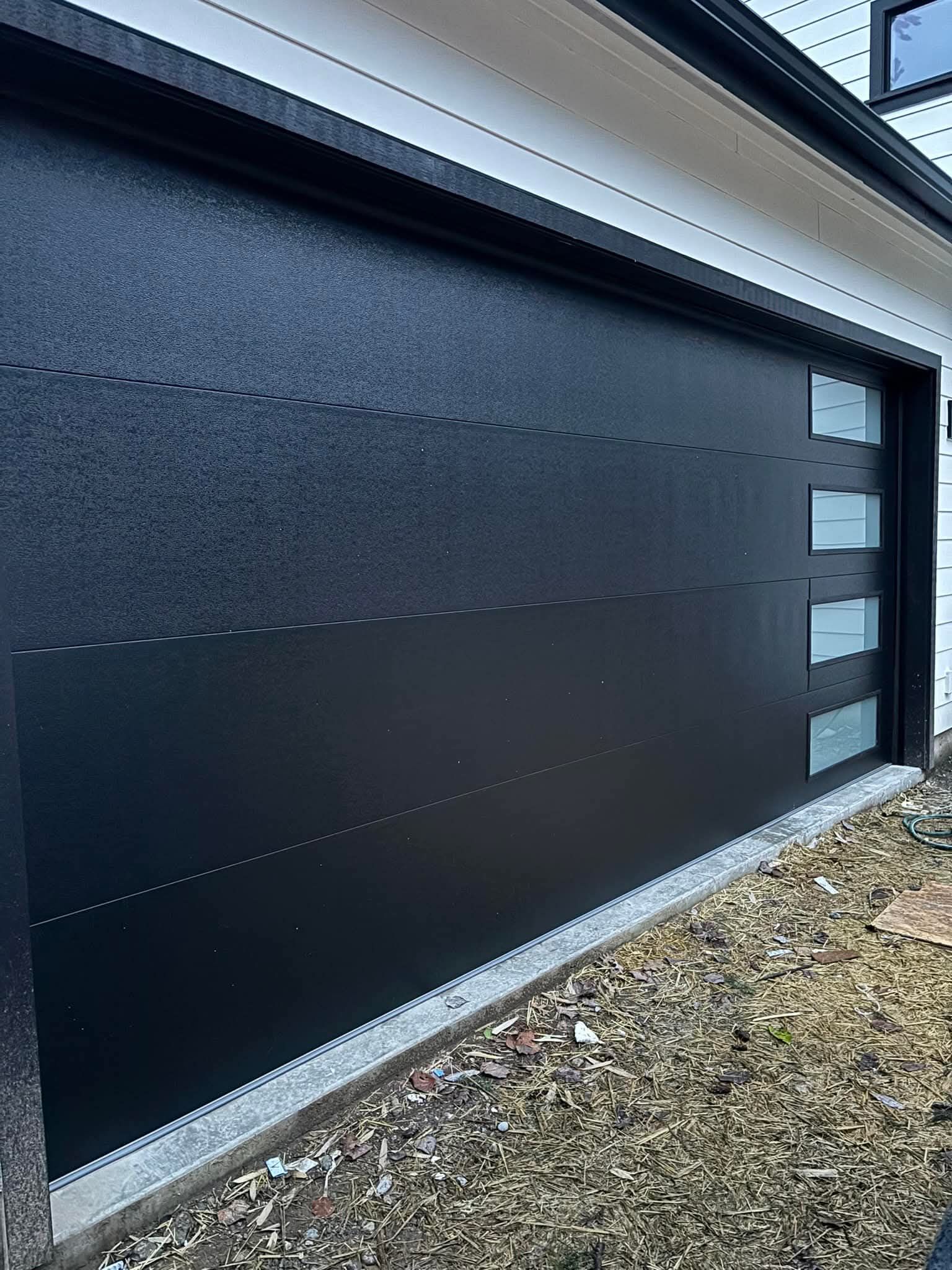 Black modern garage door with horizontal panels and frosted side windows on a gravel driveway