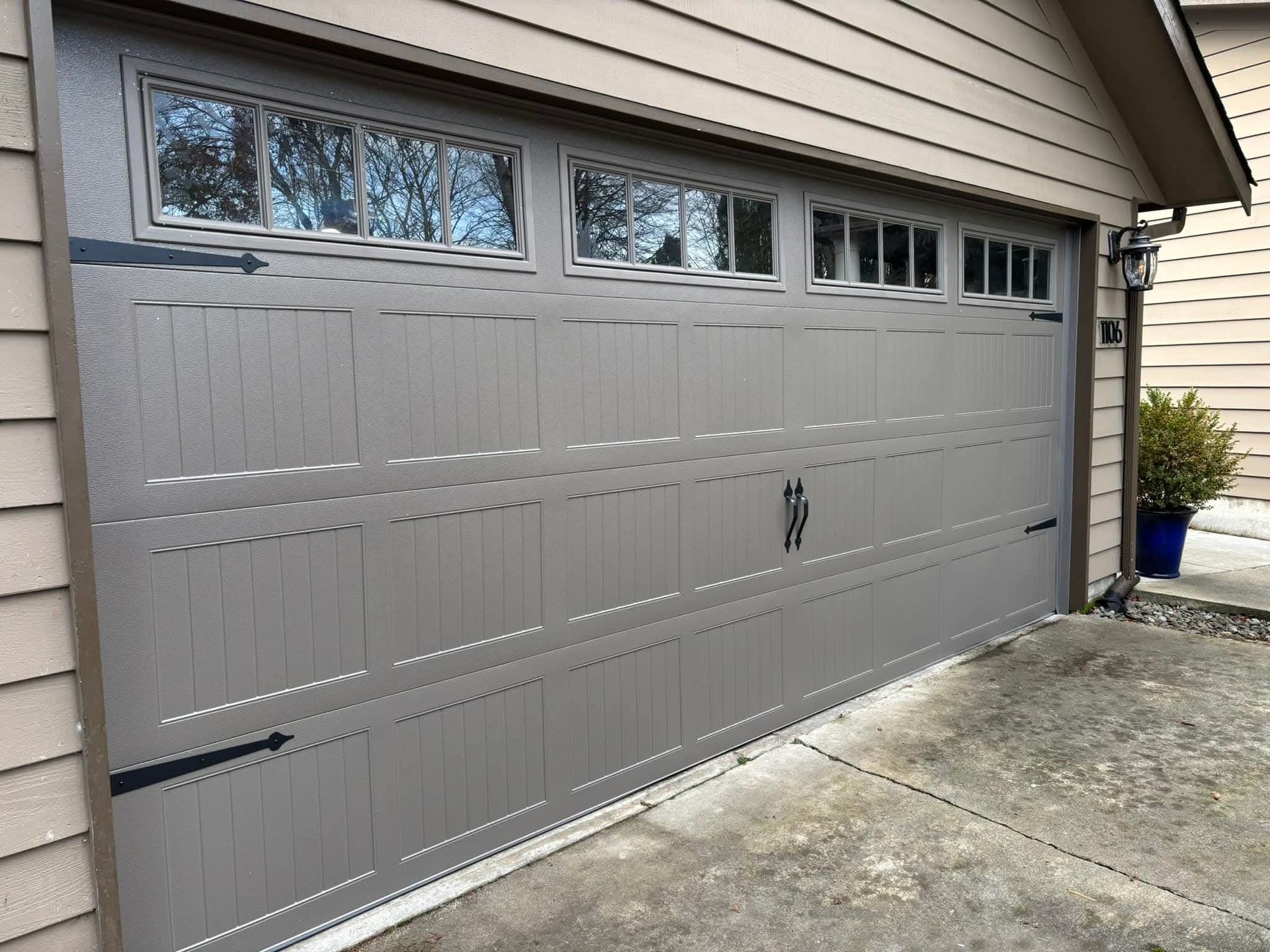 Gray garage door with small windows beside a concrete driveway and potted plant