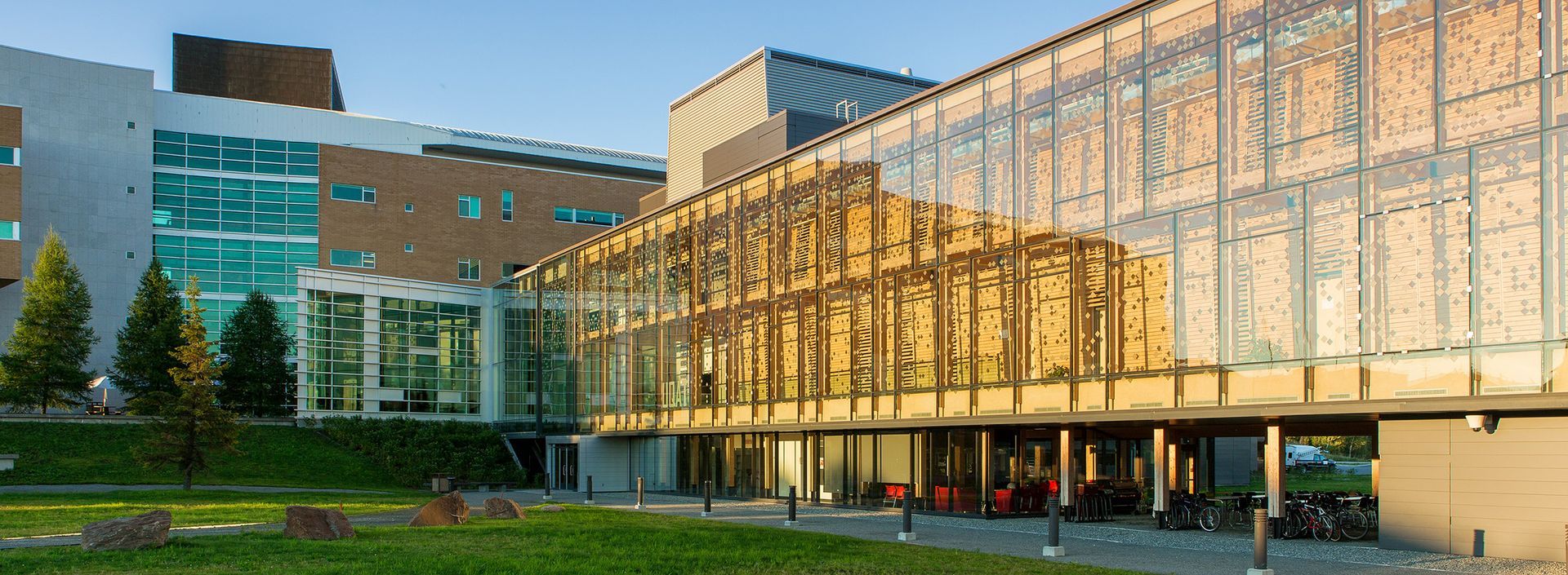 Un bâtiment moderne en verre avec une façade ornée, à côté d'un bâtiment en brique et en verre, sur une pelouse verte.