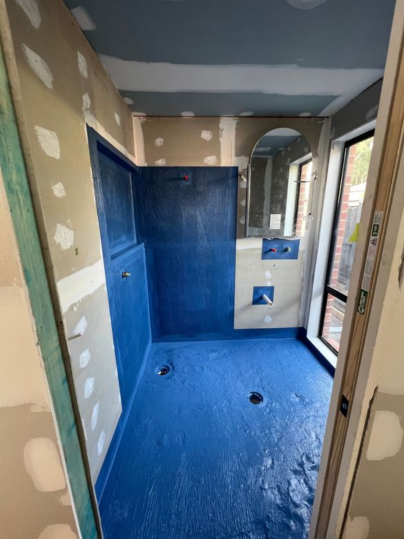 Small bathroom under renovation with blue waterproofed shower stall and unfinished walls.