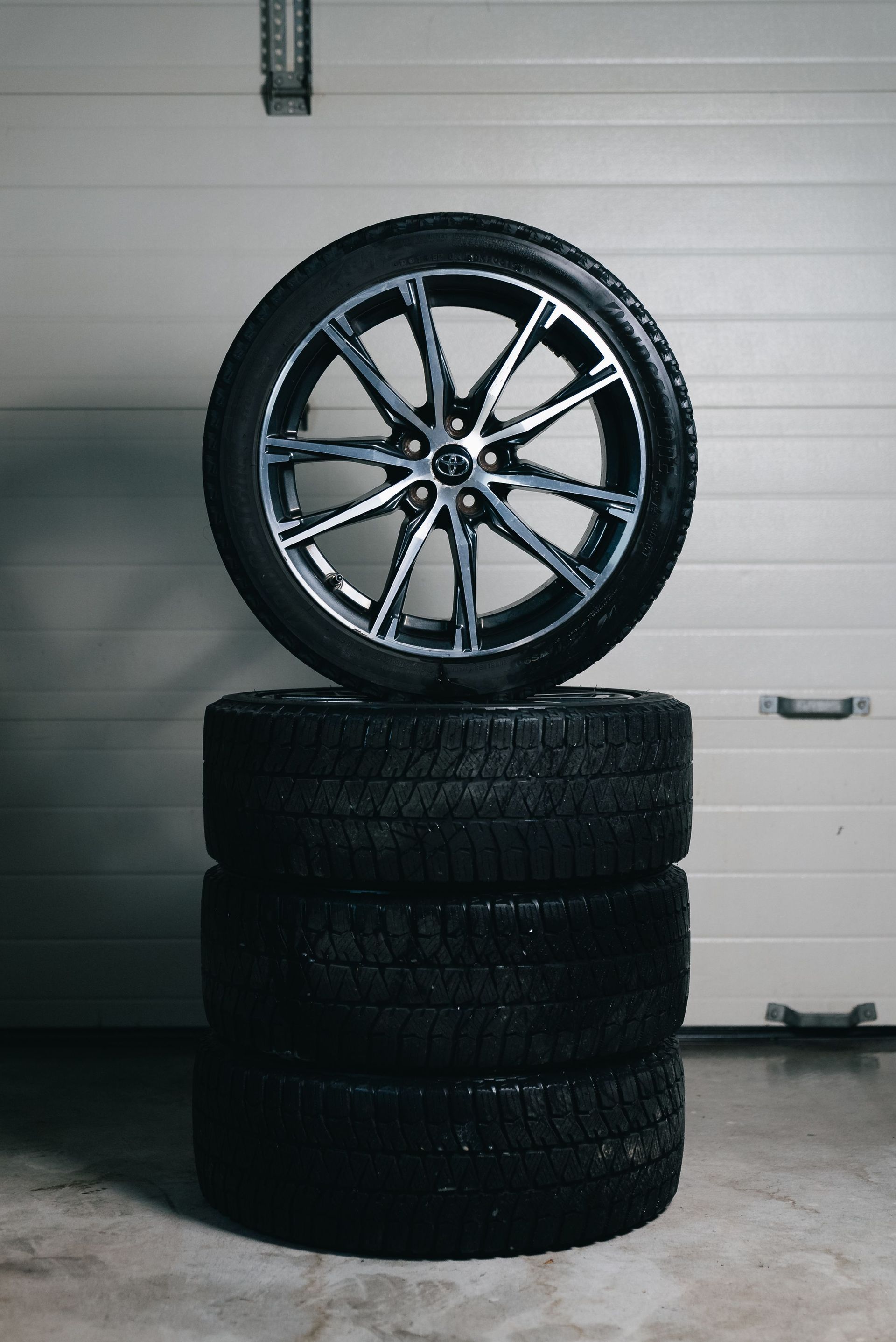 Car wheel rim balanced on three stacked black tires in a garage