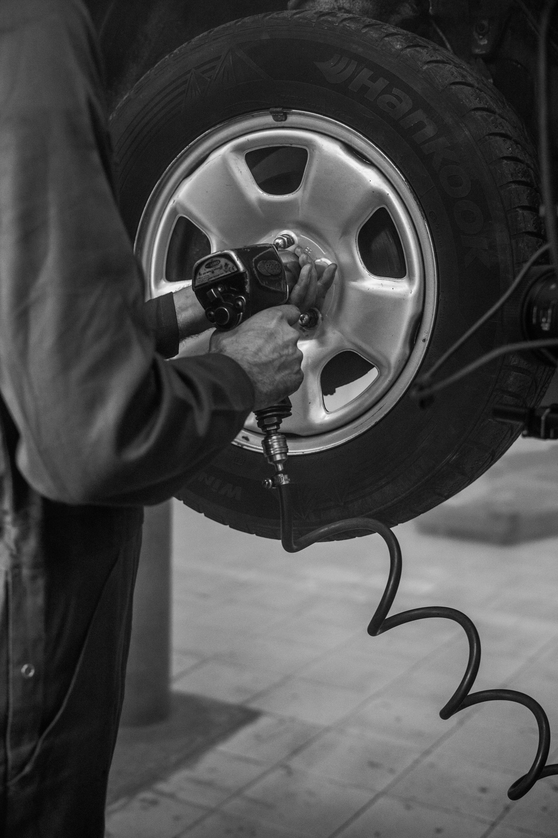Mechanic using a power tool to remove lug nuts from a car tire in a garage