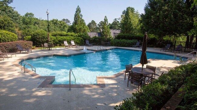 Outdoor pool surrounded by lounge chairs, trees, and greenery on a sunny day