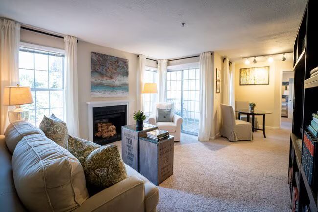 Bright living room with fireplace, cream sofa, bookshelves, and bay windows with soft beige decor