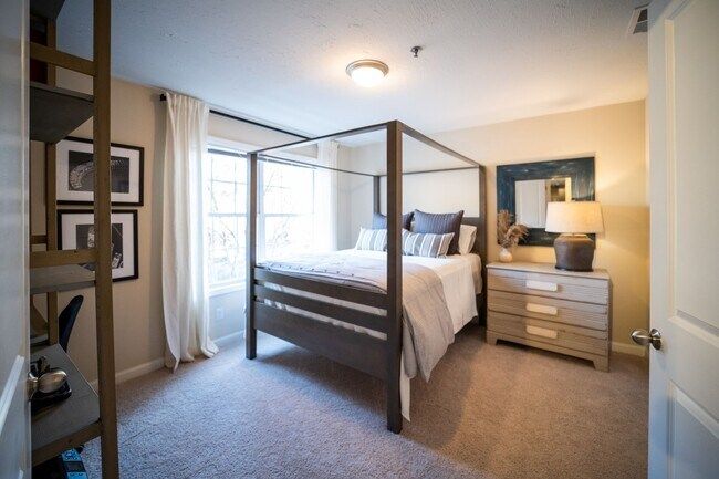 Bright bedroom with four-poster bed, dresser, lamp, and window curtains