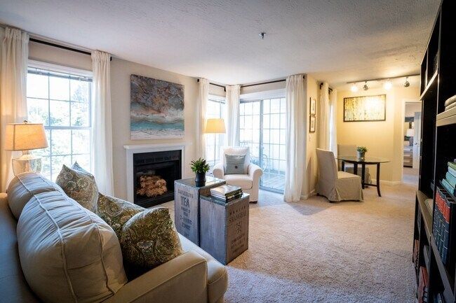 Bright living room with fireplace, beige sofa, and windows, leading to a dining area and bookshelves.