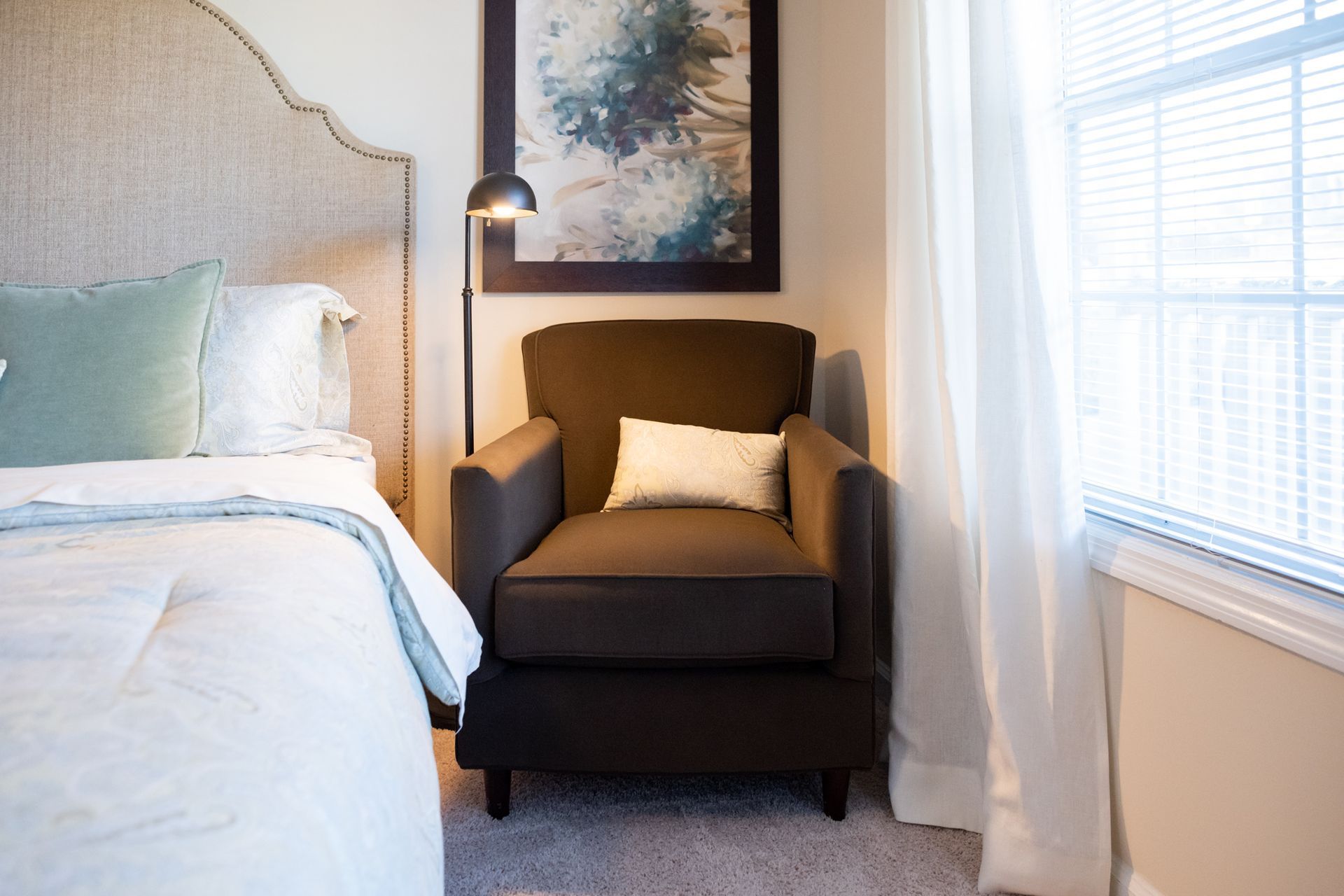 A bedroom with a bed , chair , lamp and window.