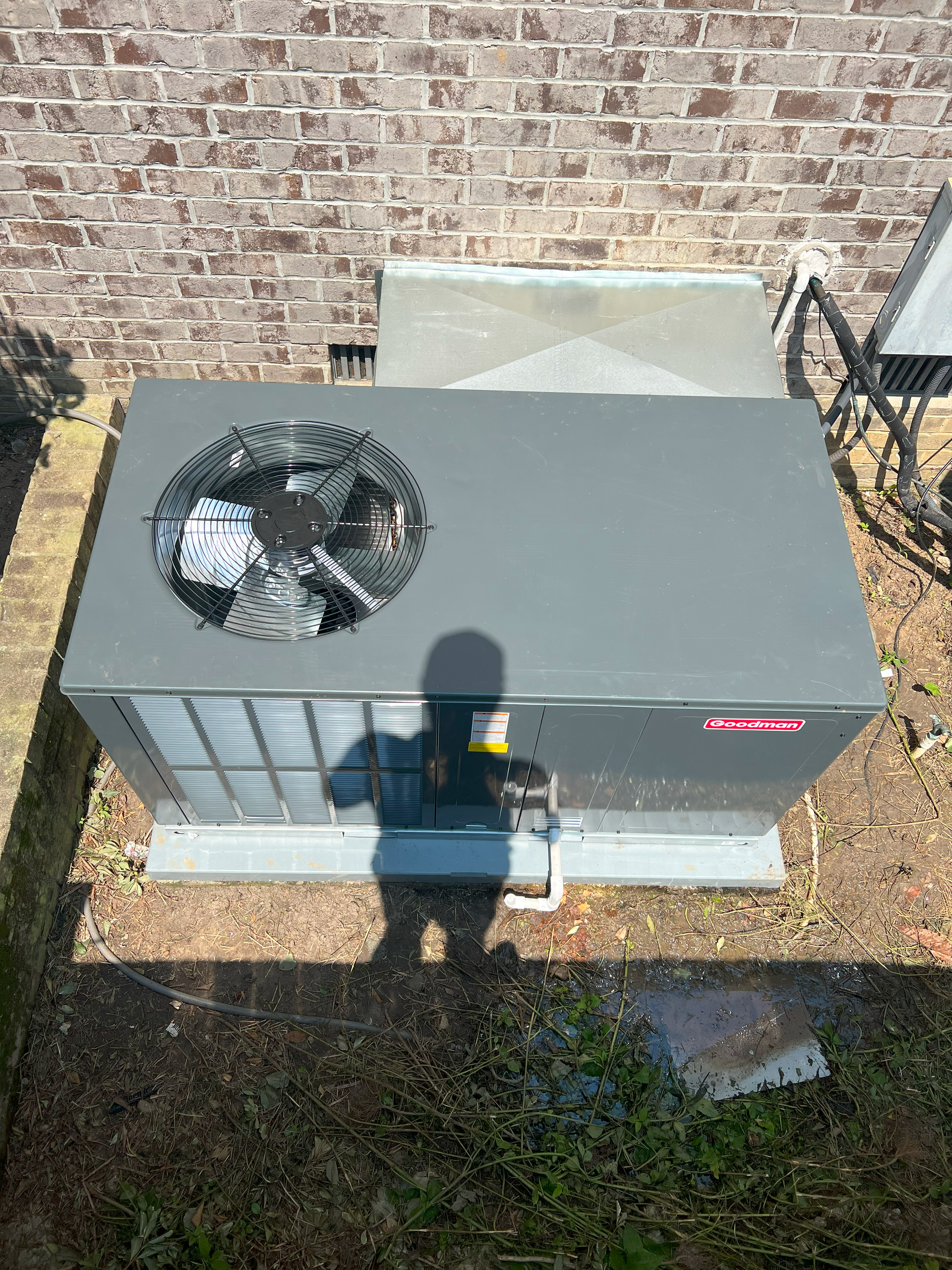 An air conditioner is sitting on the ground in front of a brick building.