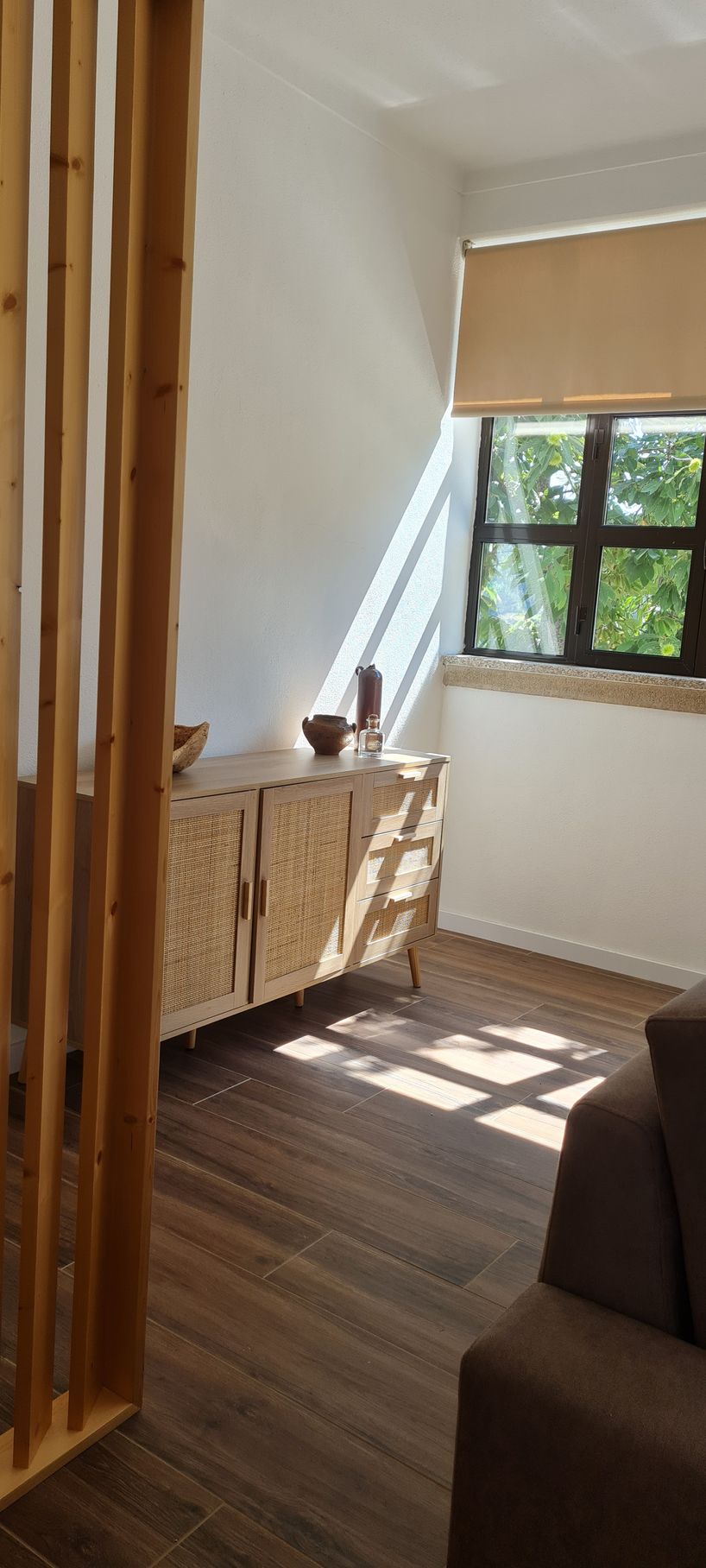 Sala de estar com um aparador, decorado com vários itens e um ambientador Castelbel. A luz do sol entra pela janela.