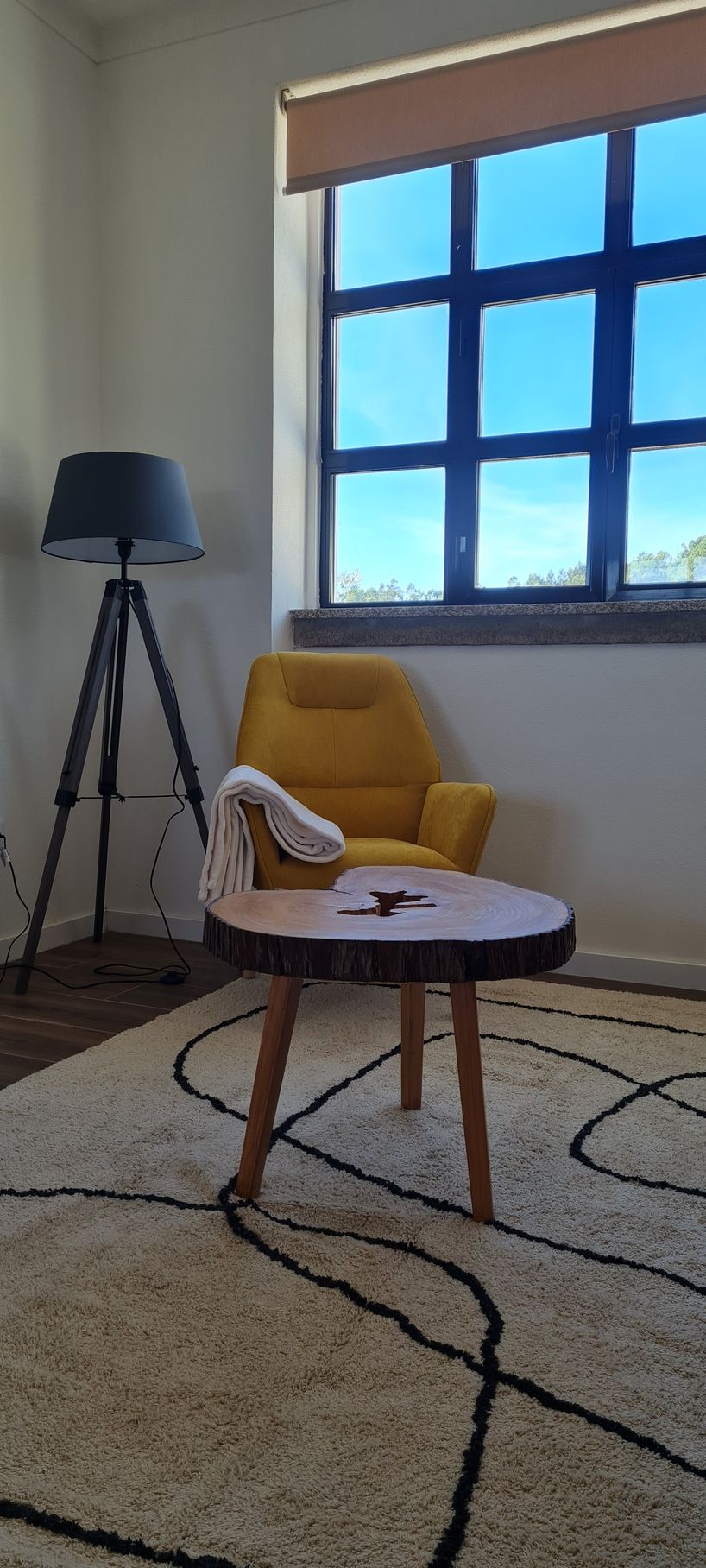 Um cadeirão de leitura amarelo, com uma manta deitada sobre um dos braços, junto de um candeeiro de pé.