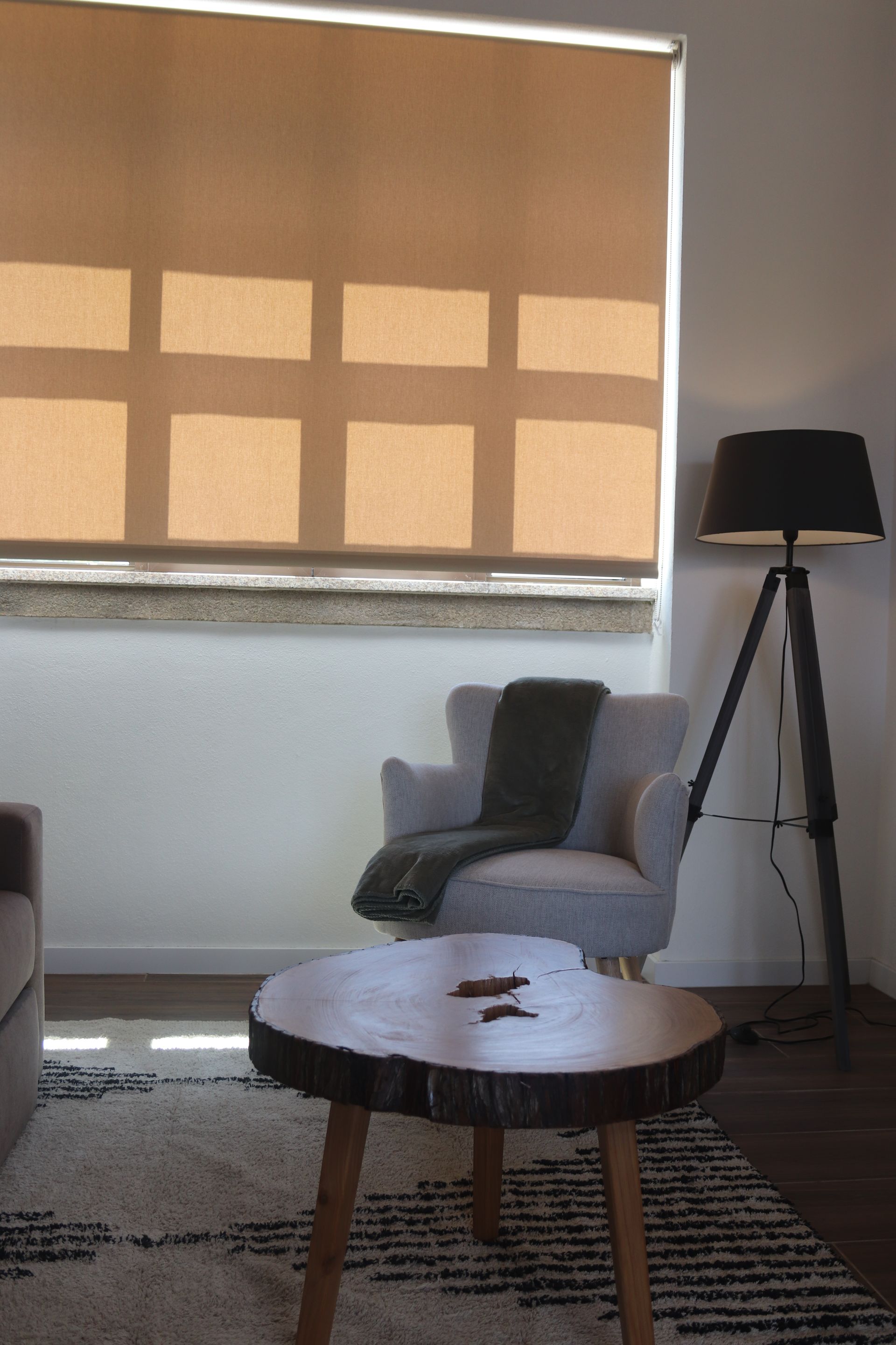 Um cadeirão de leitura cinza junto de um candeeiro, uma mesa de centro feita de cortiça e uma carpete. 