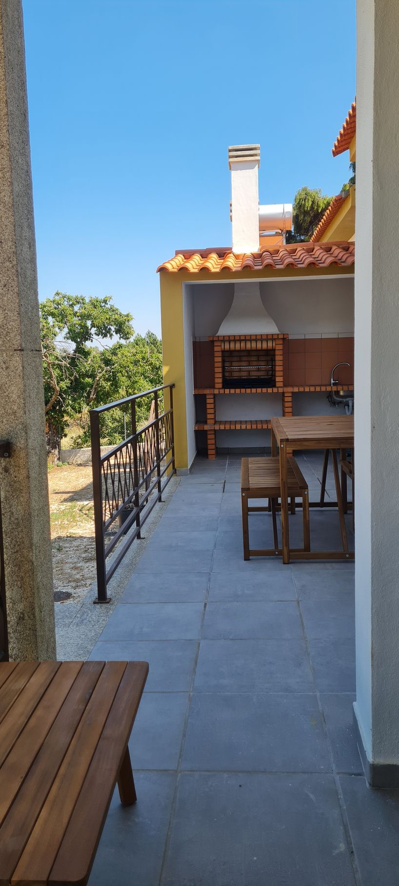 Uma churrasqueira na varanda, com uma mesa de refeição em madeira.