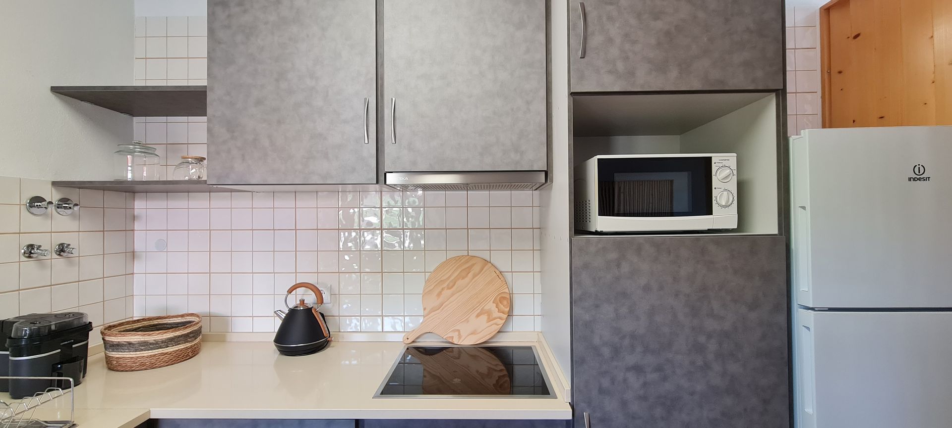 Cozinha com placa elétrica, exaustor, forno elétrico, micro-ondas, chaleira, espremedor elétrico, frigorífico e armários.