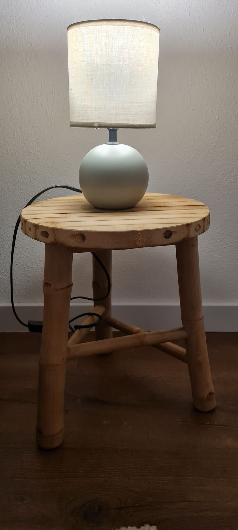 Mesa de cabeceira em bambu com um candeeiro verde aceso, com uma luz amarela confortável.