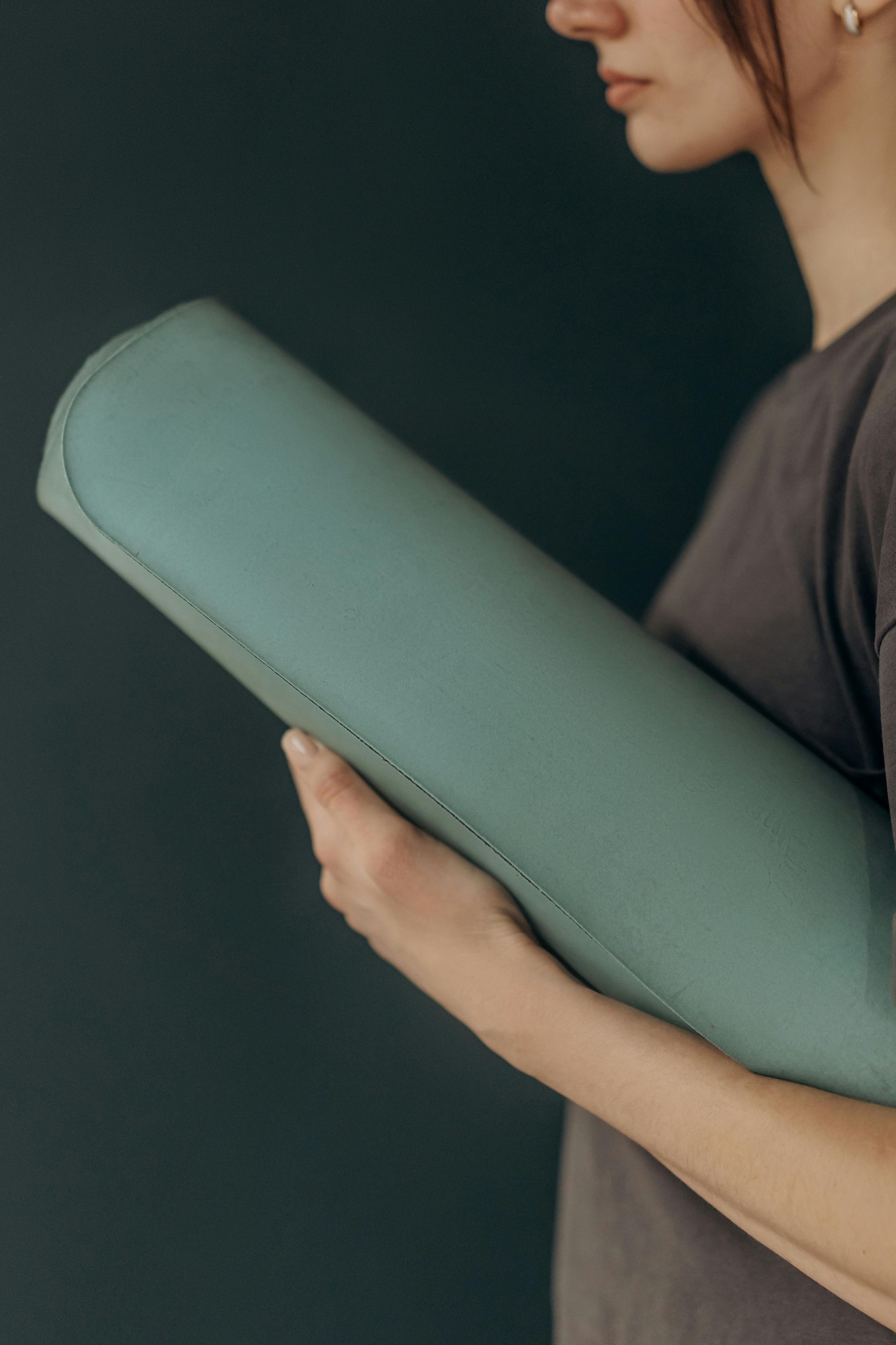 Uma senhora a segurar um tapete de yoga verde.