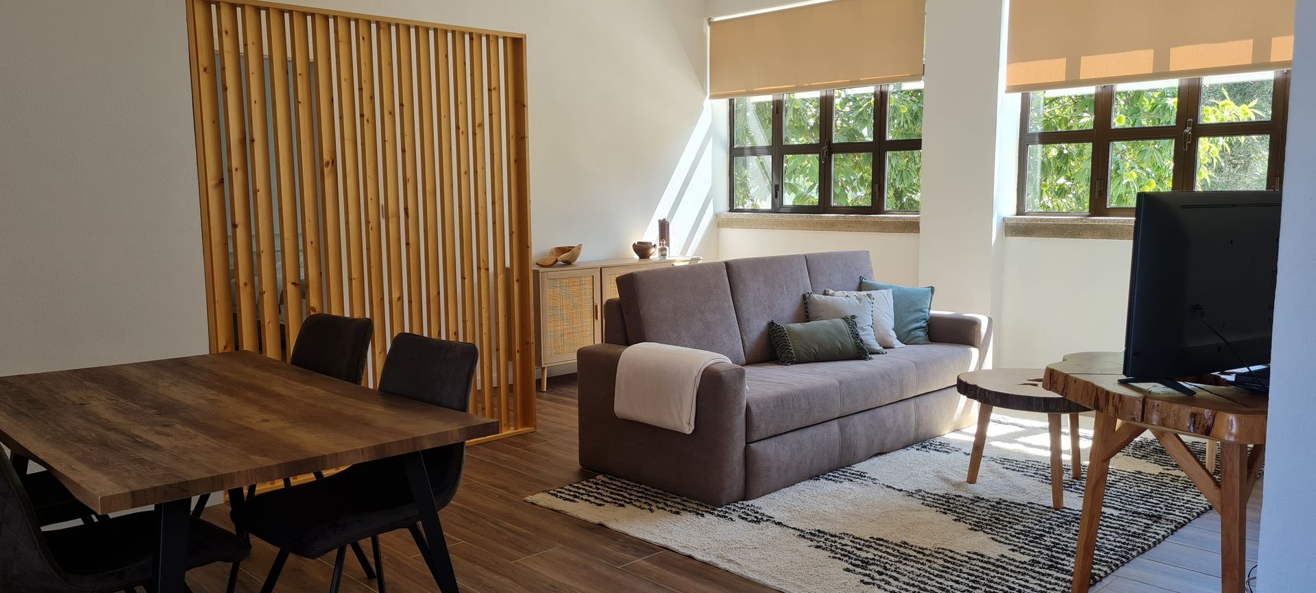 Uma sala de estar em open space, com um sofá, mesa e cadeiras. Debaixo do sofá esrá uma carpete de pêlo curto branco.