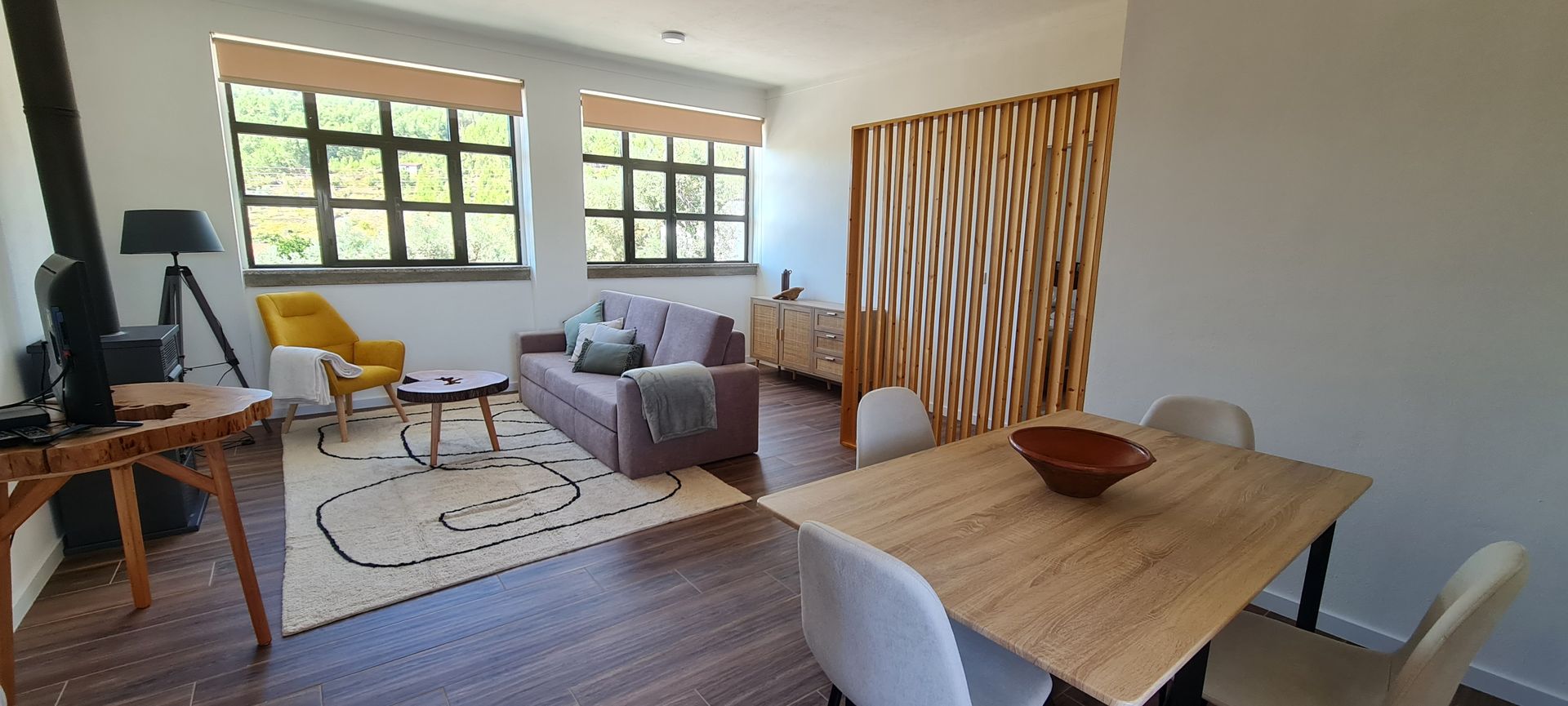 Sala de estar e jantar com uma mesa de jantar, 4 cadeiras, um sofá com almofadas, uma carpete, uma televisão e um aparador.