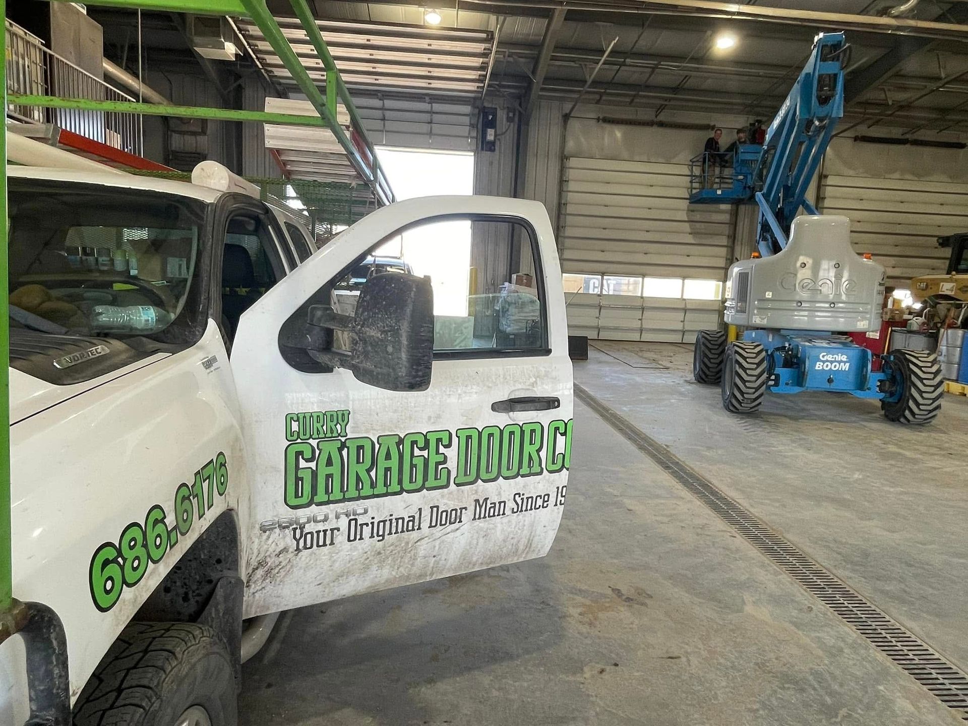 White service truck in a warehouse beside a blue boom lift.