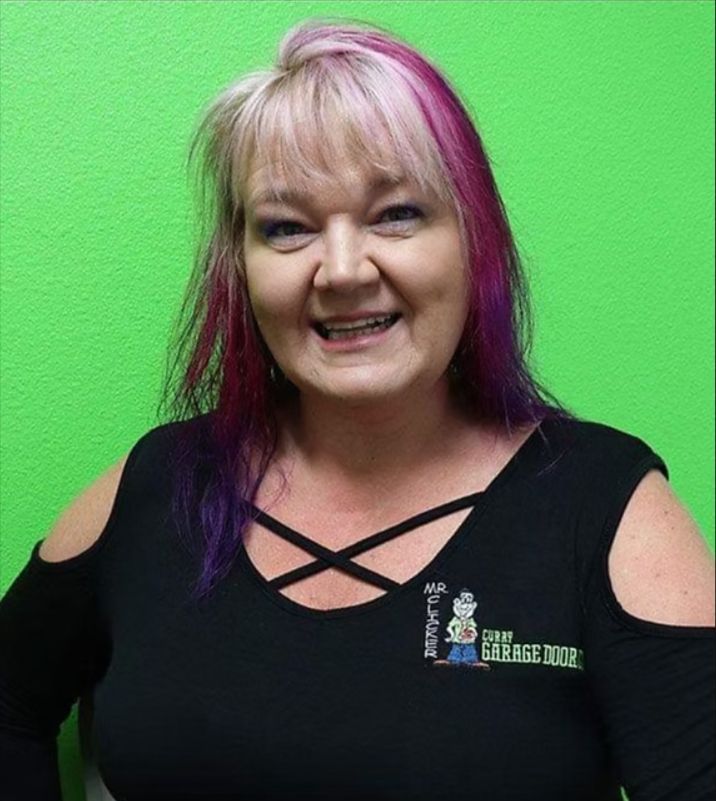 Woman smiling in black top with pink-purple hair against a bright green background