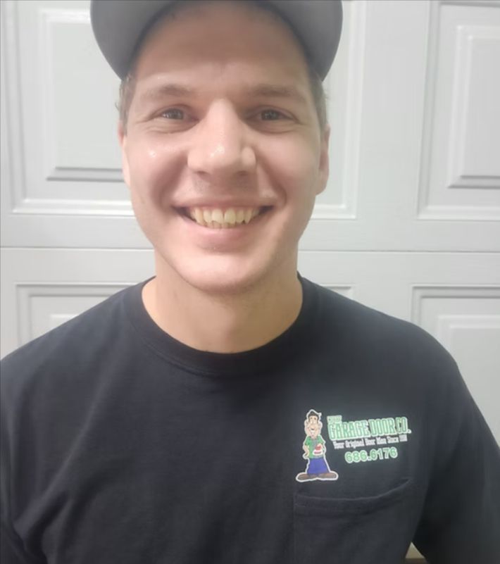 Smiling man in a black cap and black T-shirt standing before a white paneled door.