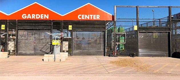 Garden center storefront with orange roof, metal gates, and a person standing near the entrance.