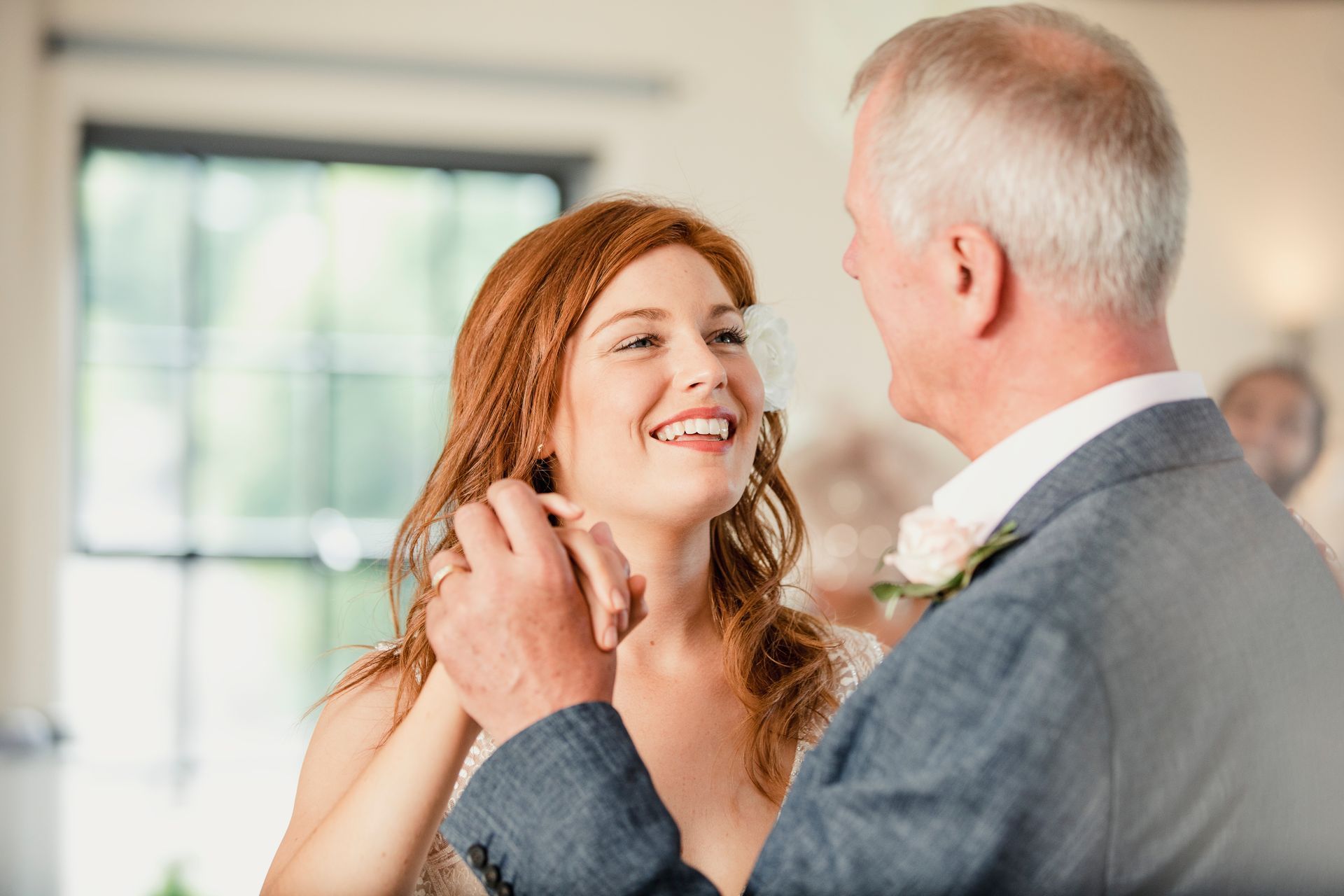 Smiling couple dancing at a wedding, with the woman in a white dress and the man in a gray suit