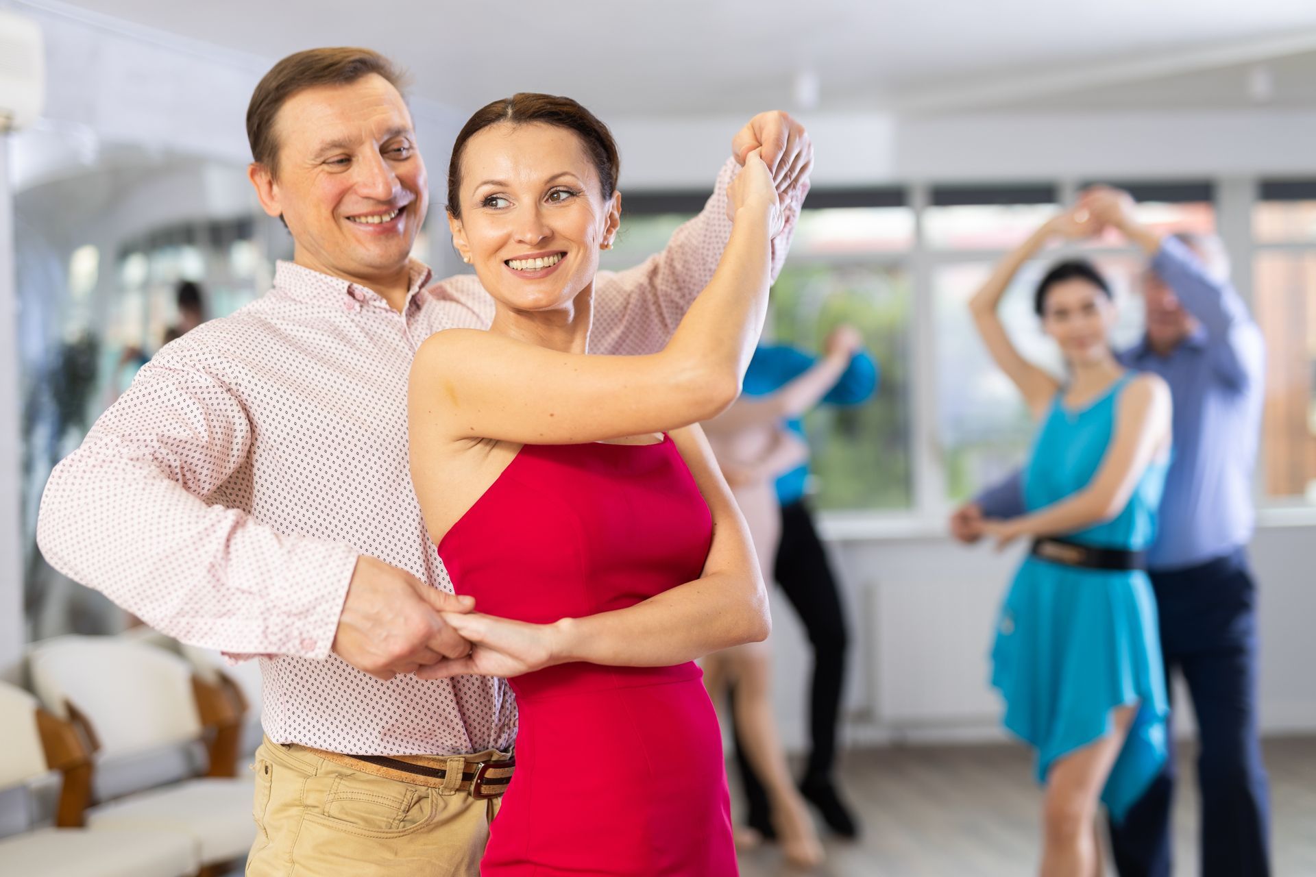 Couple dancing in a bright studio, with other dancers blurred in the background