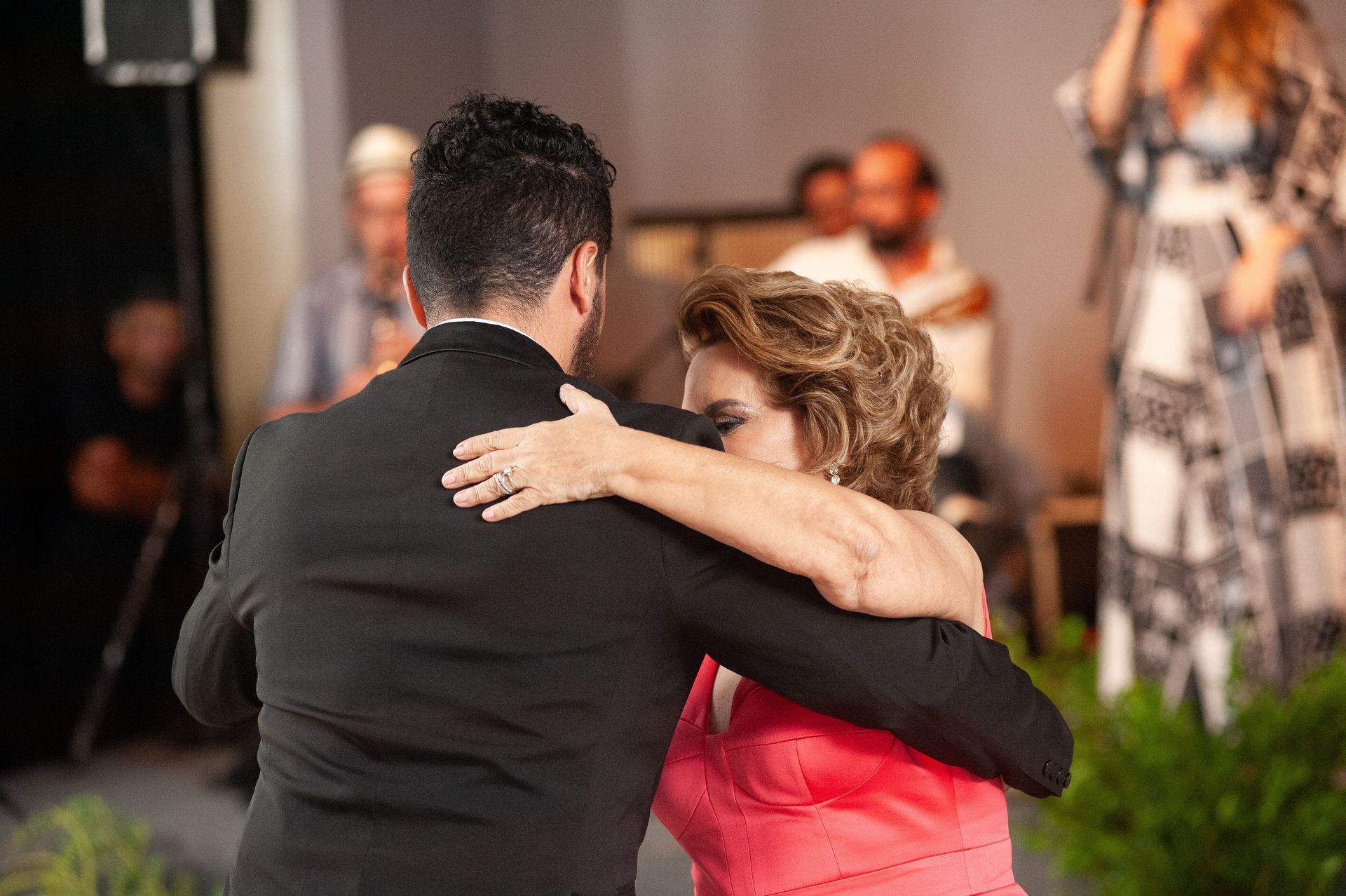Two people embracing on a dance floor at a formal event, with blurred guests in the background.