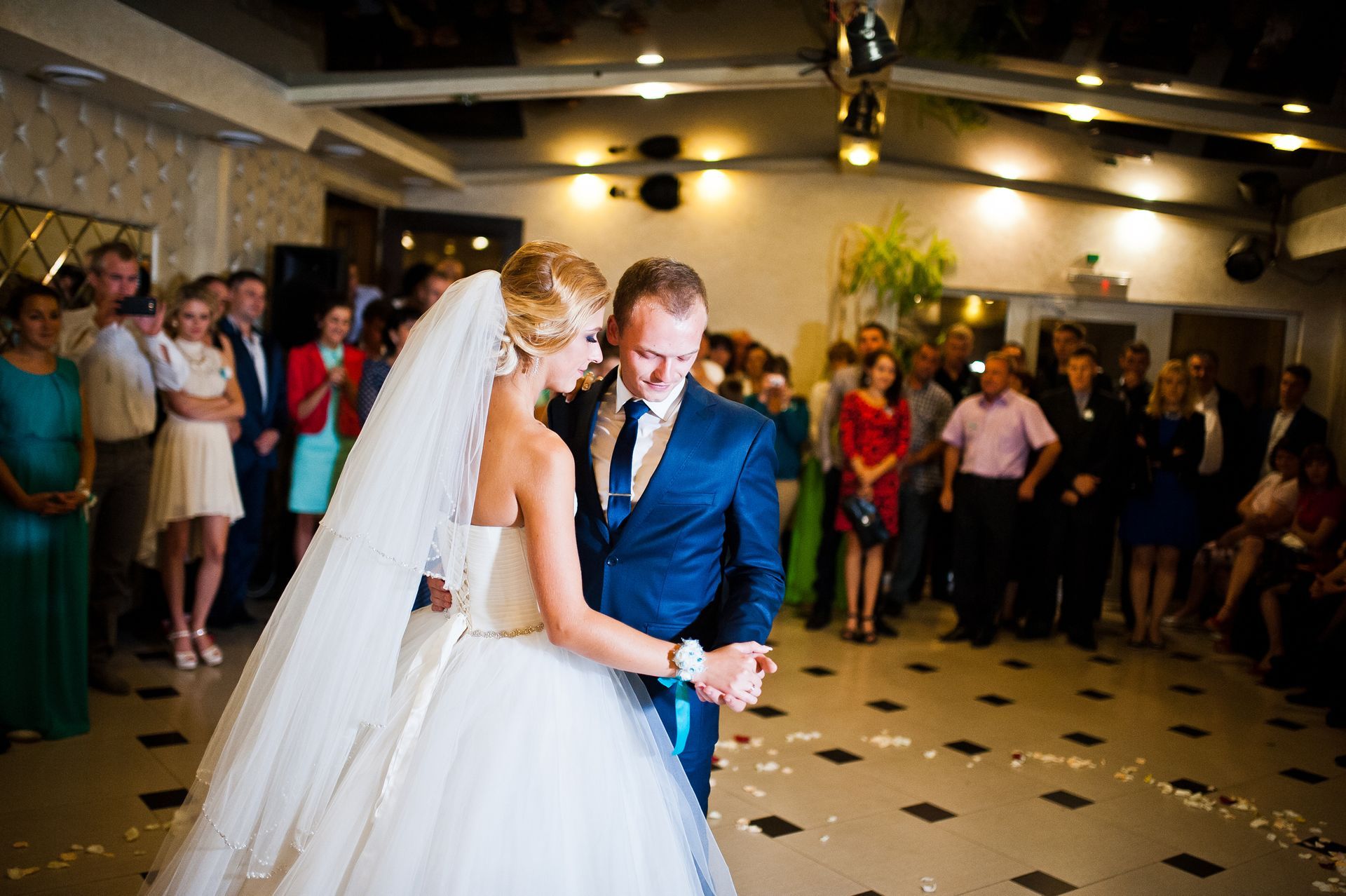 Bride and groom dancing in a reception hall with guests watching nearby