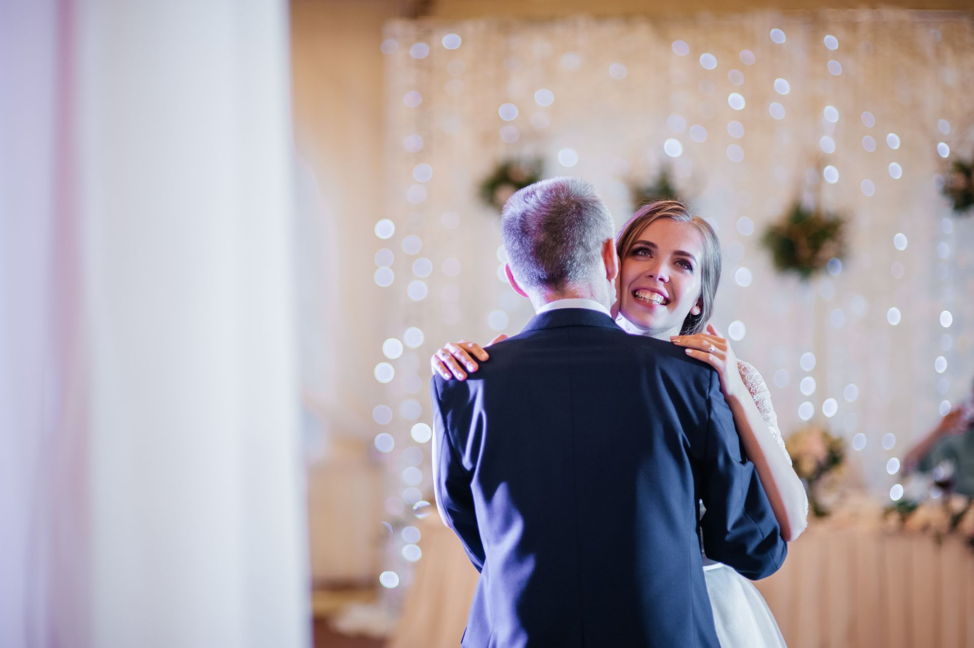Bride and partner dancing at a softly lit wedding reception, smiling amid warm bokeh lights