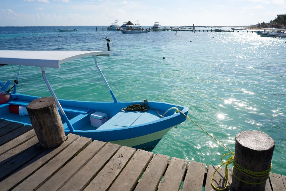 Blue boat moored by a wooden dock on turquoise water under bright sun