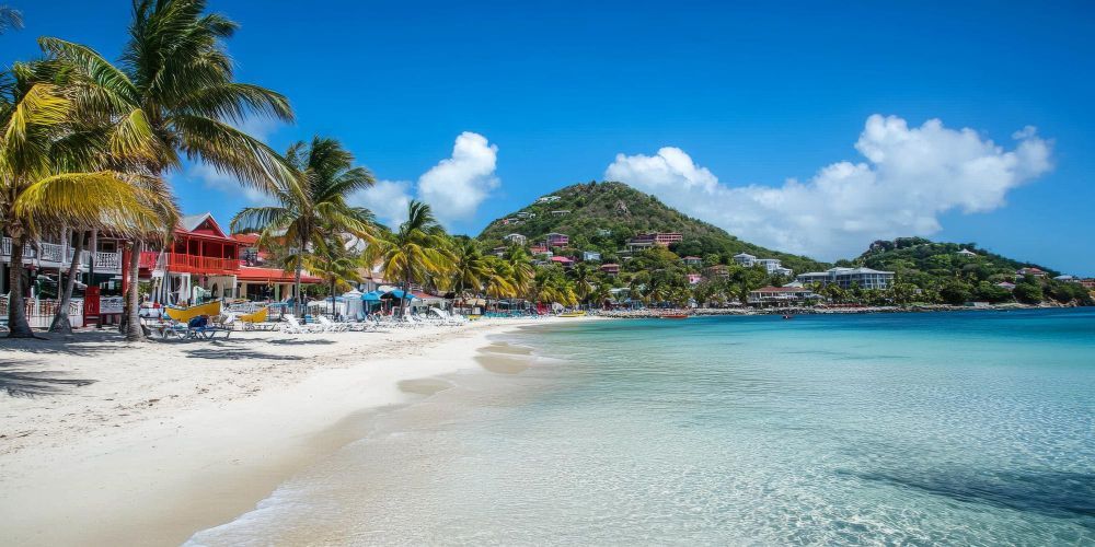 Sunny tropical beach with white sand, turquoise water, palm trees, and colorful seaside buildings